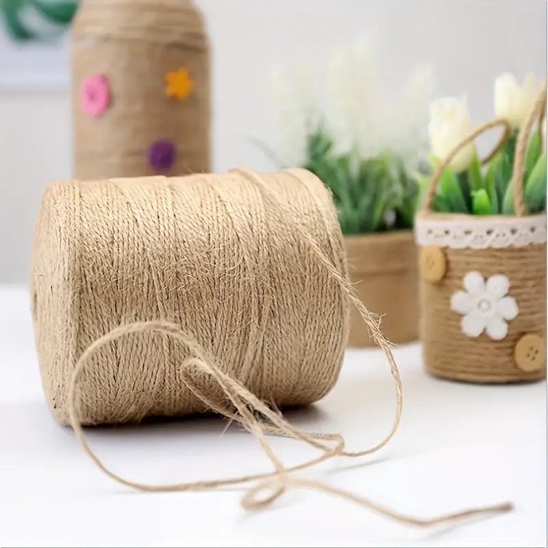 A creative workspace with colorful wrapping paper rolls, scissors, ribbon spools, gift tags, and a blank folded card on a clean wooden surface.